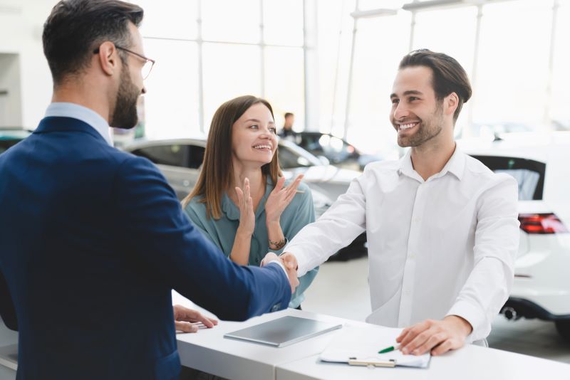 Happy couple shaking hands with a dealership representative after finalizing an extended warranty.