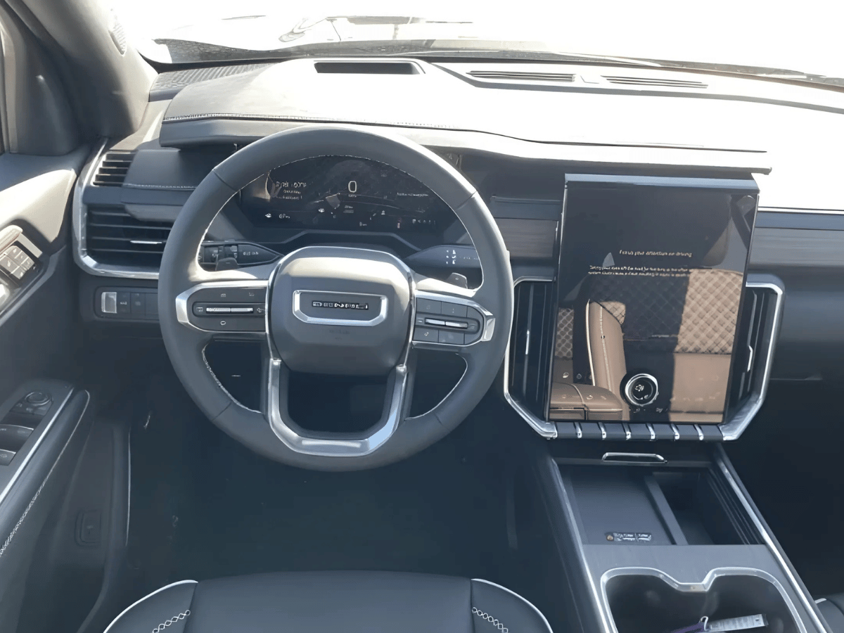 Interior view of the 2025 GMC Acadia Denali showing digital driver display, steering wheel, and vertical touchscreen with drive mode settings