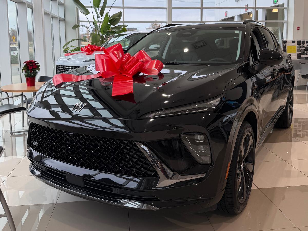 A black Buick SUV displayed inside a bright showroom with a large red bow on the hood at Crain Buick GMC of Conway.